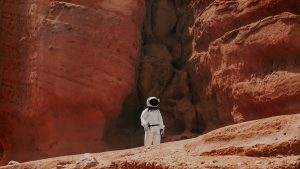 Astronaut standing in a Mars-like red rock landscape.